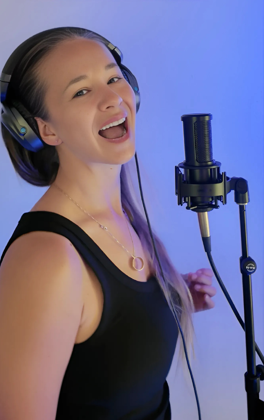 Person singing into a microphone with headphones on a blue background
